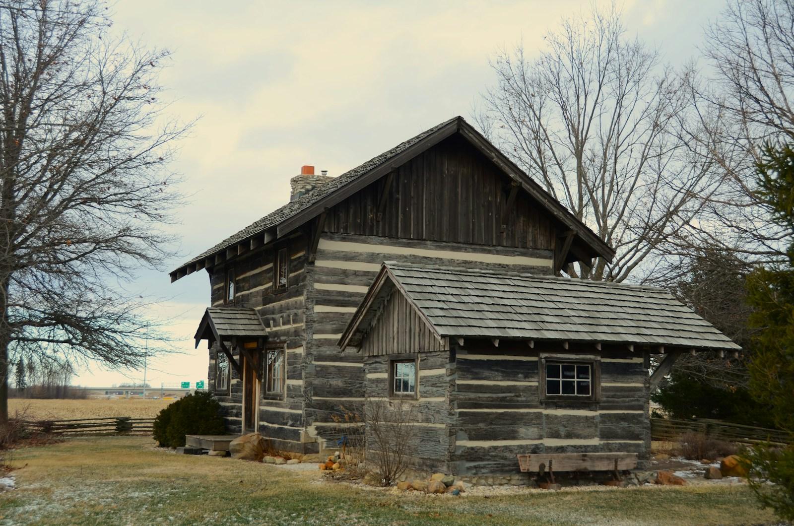 Rustic log cabin with a chimney under a cloudy sky
